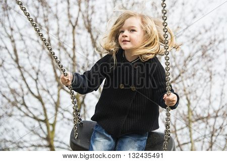 Little child blond girl having fun on a swing outdoor. Summer playground. Girl swinging high