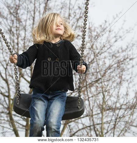 Little child blond girl having fun on a swing outdoor. Summer playground. Girl swinging high