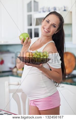 Beautiful pregnant woman with fresh fruit on the  house kitchen.