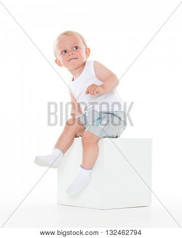 Unhappy yearling baby boy sits on cube on a white background.