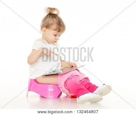 Pretty little girl with computer tablet  sits on a pink baby potty on a white background.