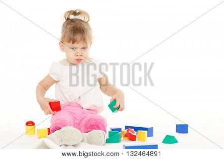 Little resentful girl plays with children blocks set on a white background. Learning toys and early development.