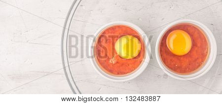 Raw eggs with tomatoes in the ramekins on the white wooden table wide screen