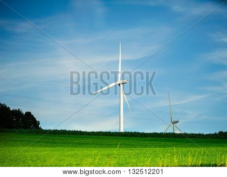 Two wind turbines - environmental protection eco tower generating electricity in green field with storm clouds in the bacground