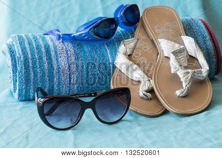 Beach towel swimming goggles sungalsses and sandals on turquoise background