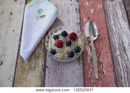 Lay flat image of homemade bircher muesli in glass dish with napkin and spoon on wooden background