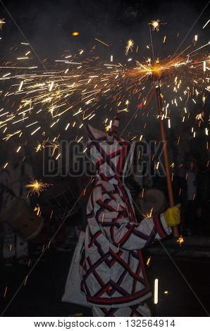 Traditional catalan spectacle called Correfocs (fire runs) or Ball de Diables (Devils' Dance). One of participants dressed as devil and dancing with lighting firework. Reus Spain. Vertical.