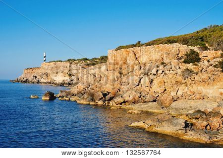 a view of the Mediterranean Sea, the Far des Moscarter lighthouse and a cliffy landscape of the northeastern coast of Ibiza Island, in the Balearic Islands, Spain