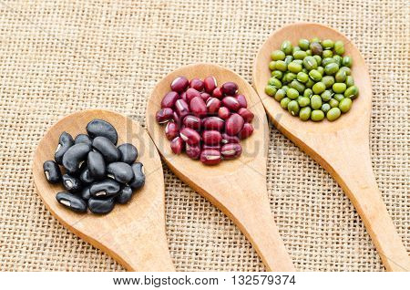 Multicolored beans in wooden spoon on sack background.