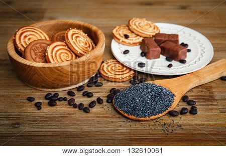 There are Cookies,Candy,Chocolate Peas,Poppy;Ceramic Plate;Tasty Sweet Food on the Wooden Background