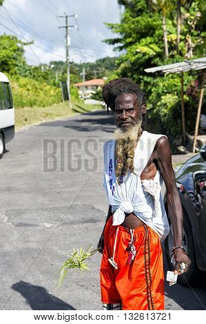 Castries st.Lucia-November 26 2015: homeless african american man with messy hair and long beard holding money and palm leaf suuny day outdoor on road