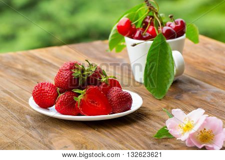Group of fresh spring fruits together cherries and strawberries. Cherries in white bowl.Strawberry on a wooden background. Red strawberries. Strawberries on green