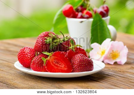 Group of fresh spring fruits together cherries and strawberries. Cherries in white bowl.Strawberry on a wooden background. Red strawberries. Strawberries on green