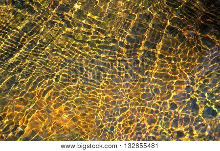 Ripples and patterns created by sunlight reflecting on a shallow golden creek bed