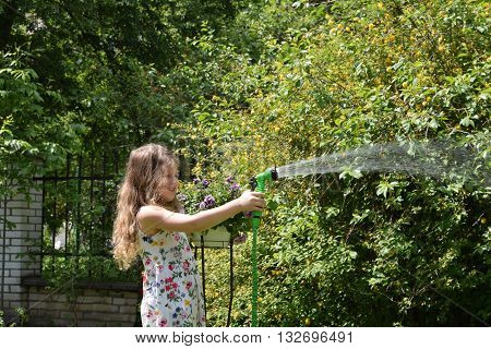 Adorable little girl playing with a garden hose on hot and sunny summer