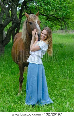Young beautiful woman in a long skirt hugs muzzle of bay horse