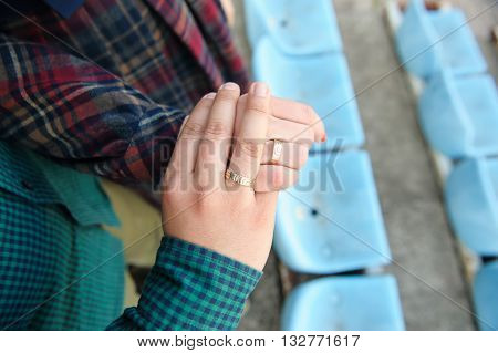 Man and woman hold hands together. Rings on the hands of the husband and wife. Couple stands between the rows of seats in the stadium. Focus on the hands with rings. View from above.