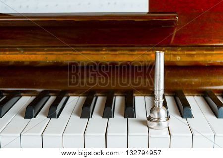 A trumpet mouthpiece upon the piano keys close up