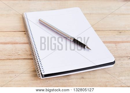Blank white notebook with pen on wood desk. shallow depth of field