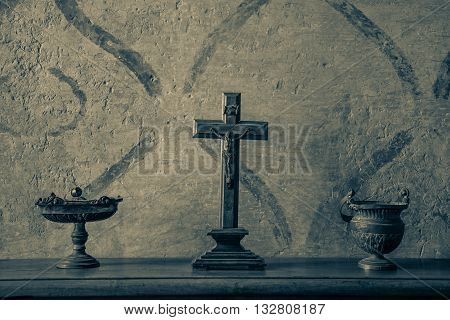 An ancient and weathered crucifix on a wood table between bronze vases