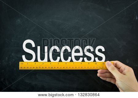 Yellow wooden ruler measures the word success on blackboard
