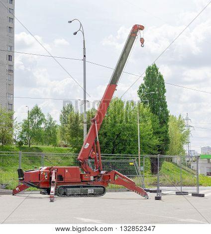 Red self propelled crane mounted on crawlers carrier with telescoping boom on an asphalt site against the backdrop of trees the sky and the urban