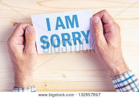 I am sorry message top view of male hands holding apologizing card