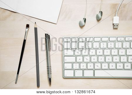 flat lay office desk with keyboard pen paper pencil earphone and usb cable on wood background