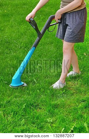 Young White Woman Holding A Corded Grass Trimmer On The Backyard Lawn At Summertime