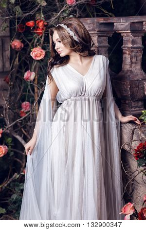 Girl in a white loose-fitting clothing on the background of the old wall with roses