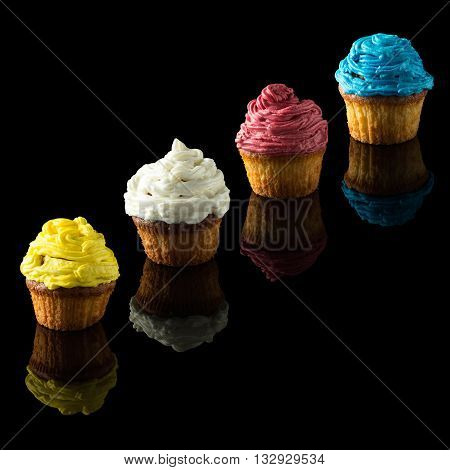 four colorful muffins on black with reflection