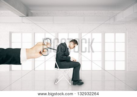 Hand activating businessman with a wind-up key on his back in white brick room. Concept of control