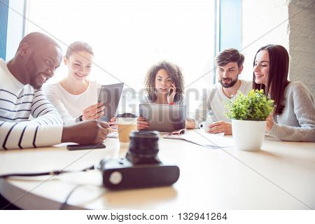 Informal workshop. Cheerful and smiling young group of people sitting together and discussing their business plan while using various modern devices