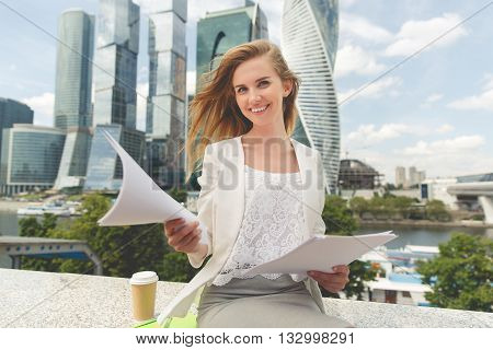 business, paperwork and people concept - young smiling businesswoman with heap of papers sitting on city bench