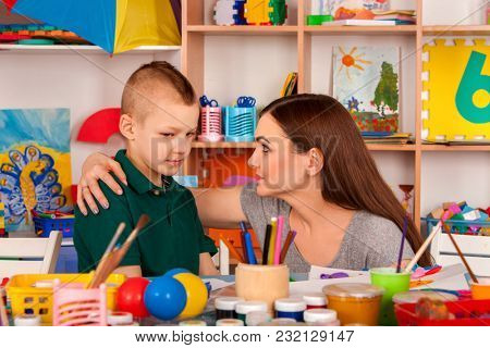 Small students girl and boy with teacher painting in art school class. Child drawing by paints on table. Mom praises son in kindergarten. Newcomer in children's team.