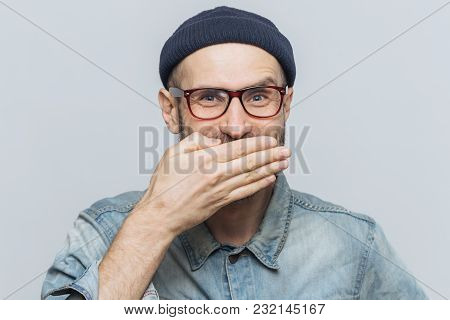Funny Man With Attractive Look Giggles Or Laughs Joyfully, Covers Mouth With Hand, Tries To Stop Fee