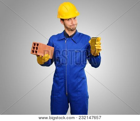 Engineer Holding Brick And Goldbar On Grey Background