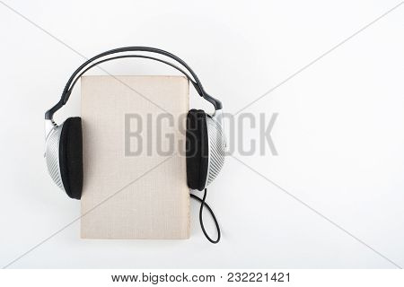 Audiobook On White Background. Headphones Put Book, Empty Cover, Copy Space For Ad Text. Distance Ed
