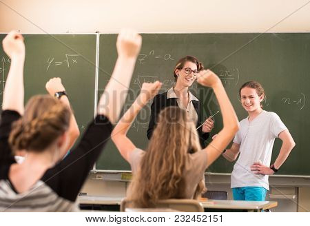 Teacher or docent or educator standing while lesson in front of a blackboard or board and educate or teaching students or pupils or mates, which notify and learn in a school or class