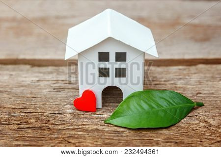 Miniature White Toy Model House With Green Leaves And Red Hearts On Wooden Backgdrop. Eco Village, A
