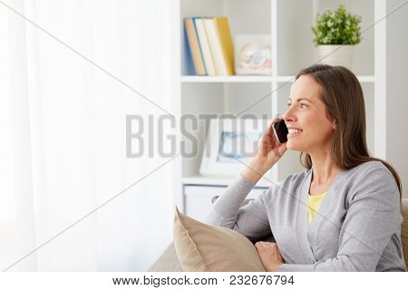 people, technology and communication concept - happy middle-aged woman calling on smartphone at home