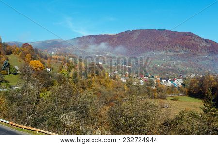 Autumn Carpathian Mountains Landscape With Multicolored Trees And Small Hamlet On Slope, And Misty C
