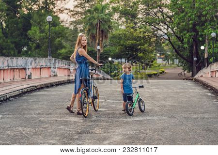 Happy Family Is Riding Bikes Outdoors And Smiling. Mom On A Bike And Son On A Balancebike.