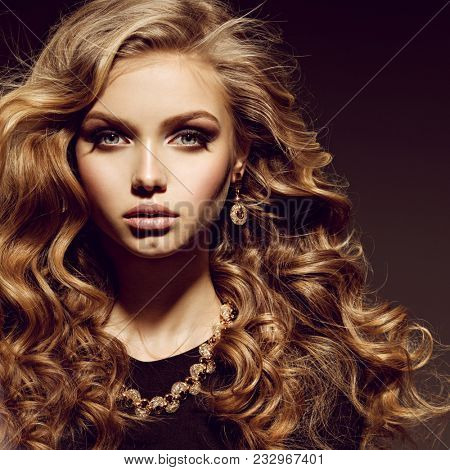 Beautiful woman with long curly hair and gold jewelry posing at studio 