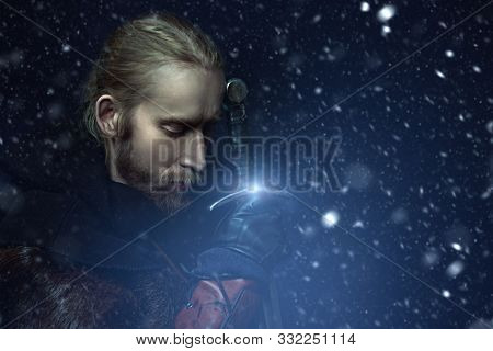 Close-up portrait of a medieval knight in armour and with a sword over winter background. Historical reenactment. Copy space.