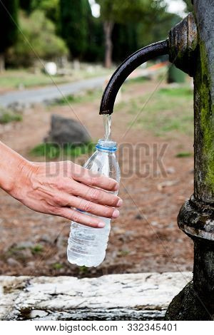 closeup of a young cacausian man filling a plastic bottle with water from a drinking fountain at the Via Appia Antica road in Rome, Italy