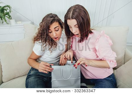 Two Amazing Friends Sitting On The Sofa, Looking In One Of The Packets From The Shop, Surprised By S