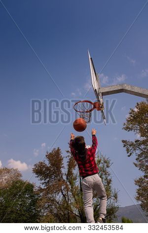 Rear View Of A 8-9 Years Old Boy, Mid Air, Shooting Jump Shot On Basketball Court. The Child Has Bro