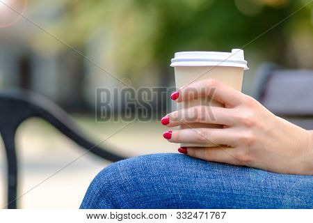 Girl In Hand With Manicure Holds Aromatic Tasty Coffee In A Disposable Cup On A Bench On A Sunny Day