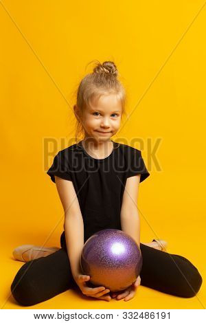 Gymnast Girl In Black Trico Full Height Sits On A Half Page With A Sports Ball Isolated On A Yellow 
